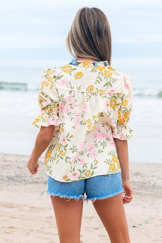 Woman wearing a floral blouse and denim shorts on a beach.