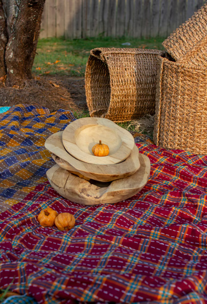 Decorative stack of wooden plates with pumpkins on a colorful plaid blanket outdoors.