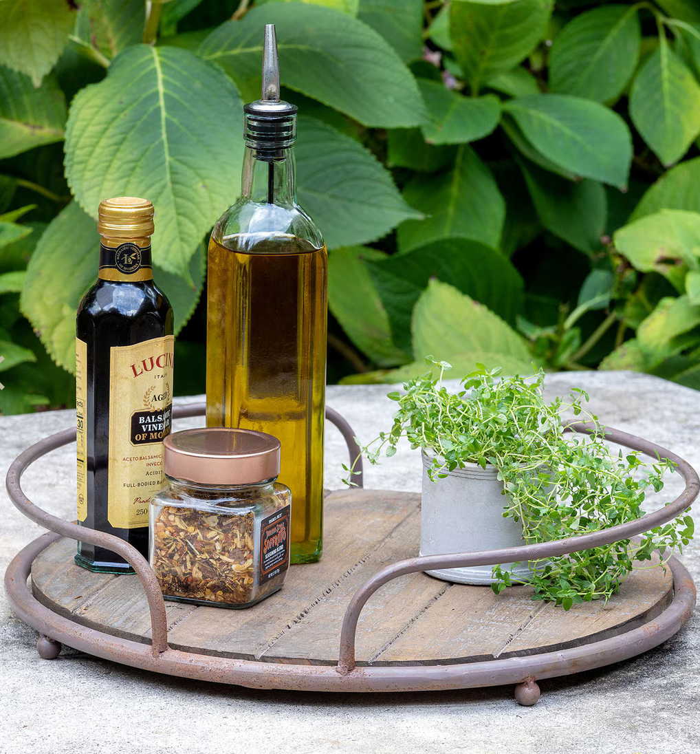 Decorative tray with bottles, a jar, and plants on a table outdoors.