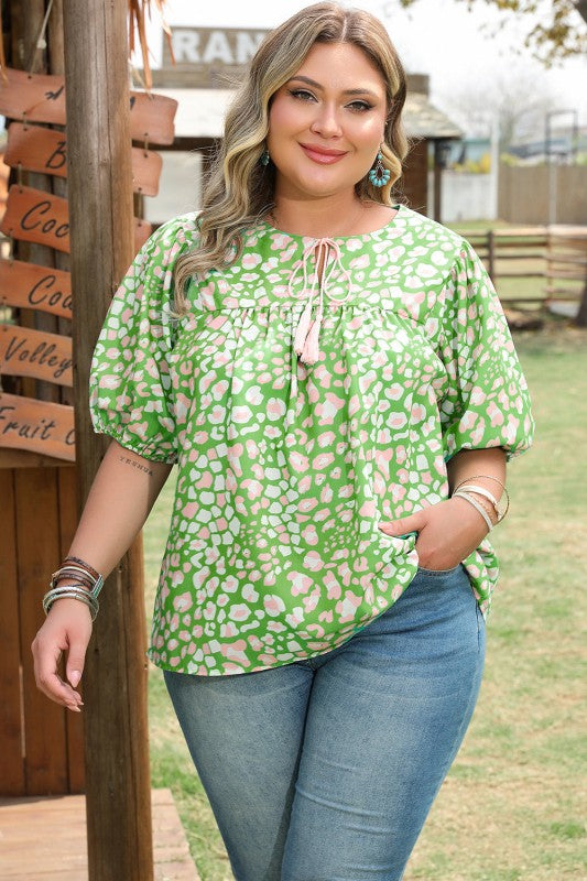 Woman wearing a green floral blouse and blue jeans standing outdoors.