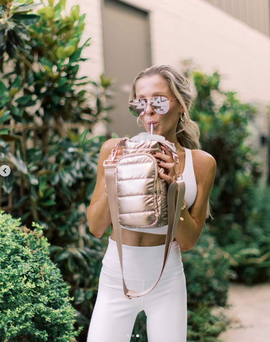 Woman holding a pink backpack and drinking from a straw outdoors