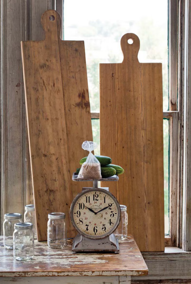 Vintage clock on a wooden surface with large wooden cutting boards and jars in the background.