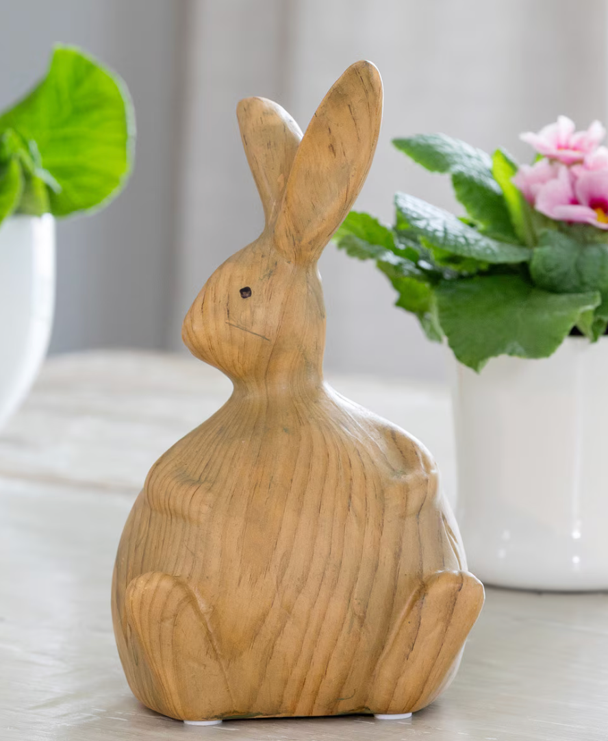 Wooden rabbit figurine on a light surface with plants in the background