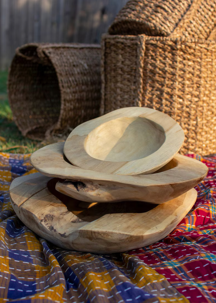 Stack of wooden bowls on a colorful fabric with woven baskets in the background