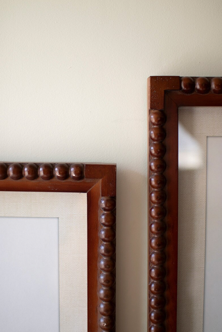 Two wooden mirrors with decorative frames on a plain wall.