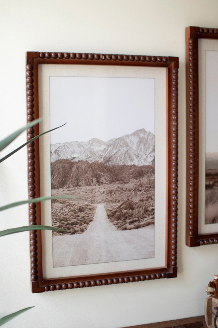 Framed landscape print of a snowy mountain scene on a wall.