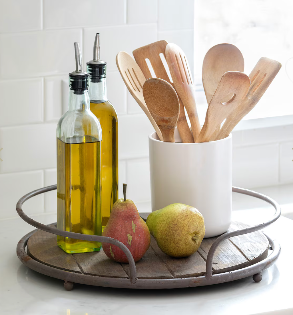 Kitchen scene with olive oil bottles, wooden spoons, and pears on a tray.
