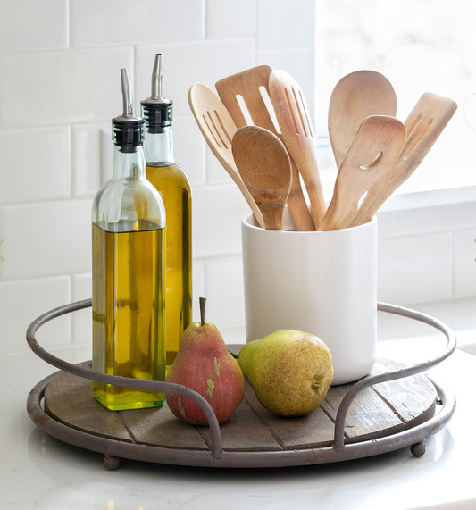 Kitchen scene with olive oil bottles, wooden spoons, and pears on a tray.