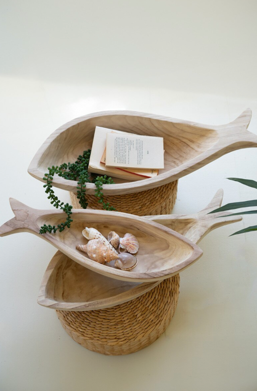Wooden fish-shaped trays with seashells and a book on a white background