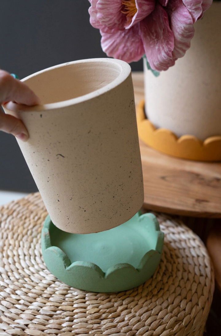 Ceramic cup being held over a green ceramic stand on a woven surface with a blurred background