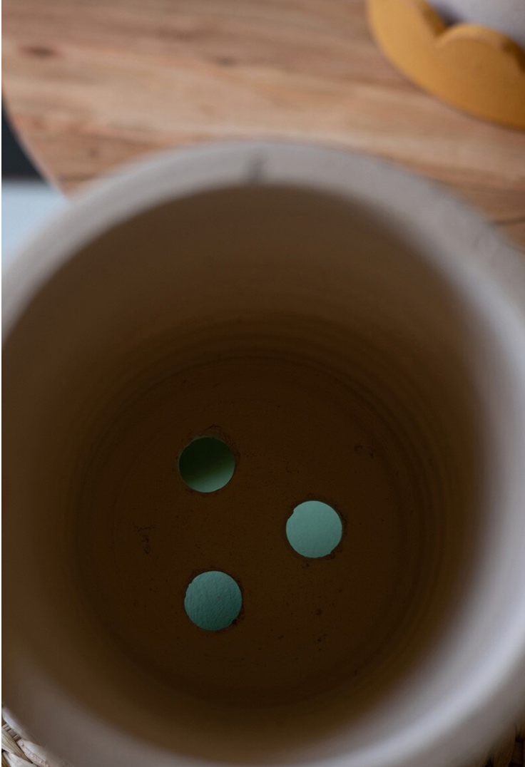 Close-up of a ceramic pot with three green stones inside on a wooden surface.