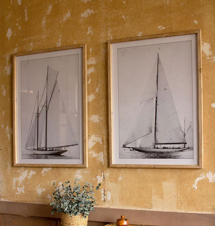 Two framed black and white sailboat prints on a textured yellow wall.