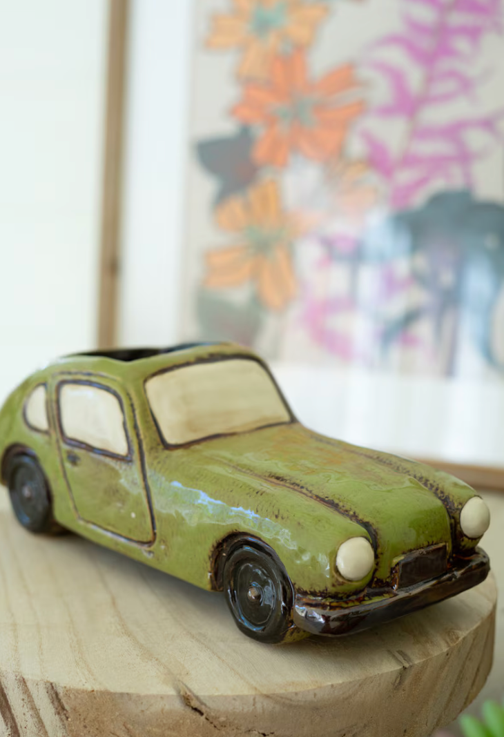 Vintage-style toy car on a wooden surface with a colorful abstract painting in the background