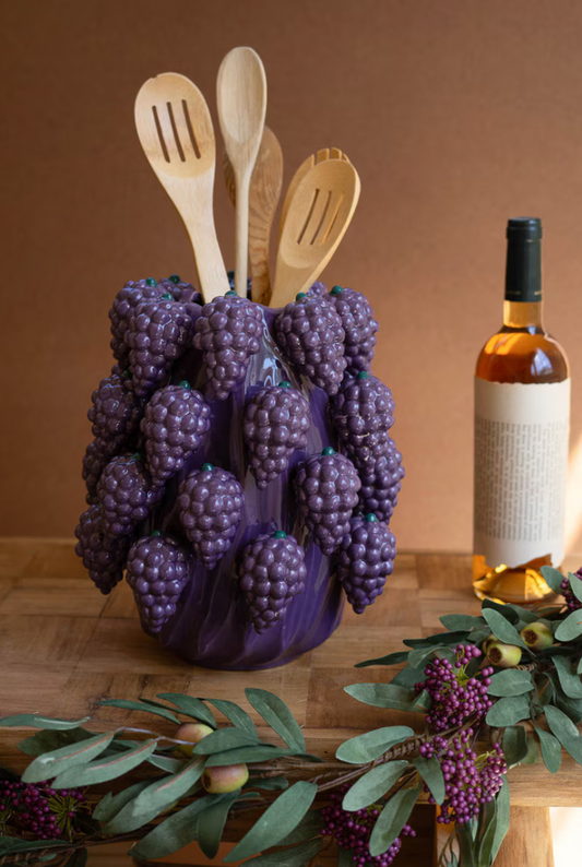 Grape-shaped utensil holder with wooden spoons on a wooden surface with a bottle of wine in the background.