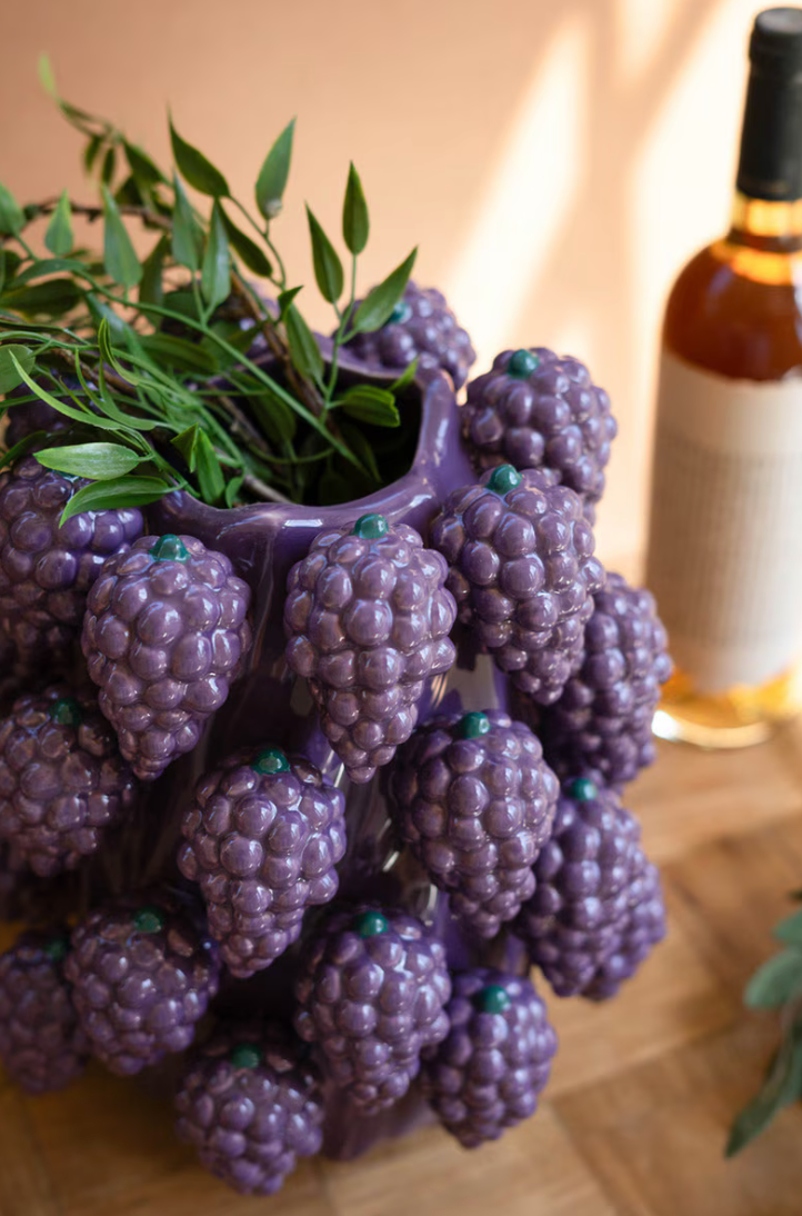 Vase shaped like a cluster of purple grapes with green leaves on a wooden surface.