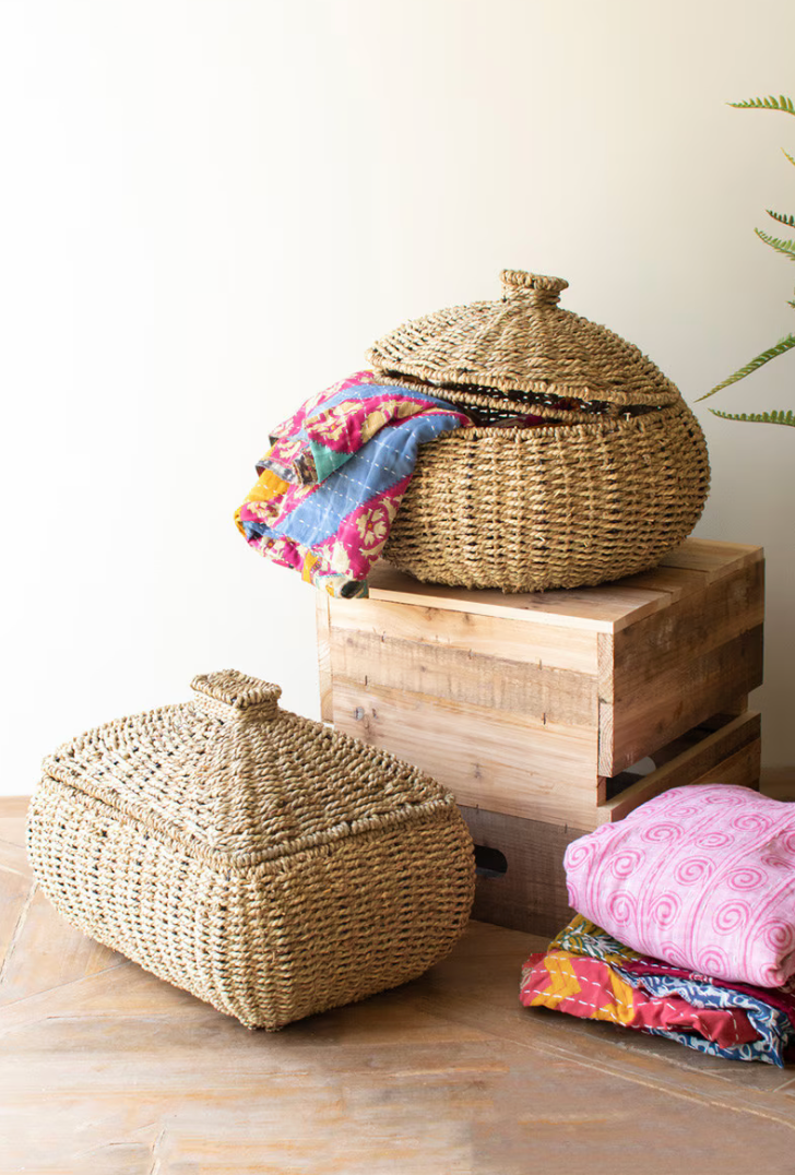 Woven baskets with lids on a wooden surface, surrounded by colorful fabric cushions.