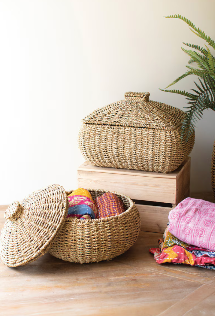 Woven baskets with lids on a wooden surface, containing colorful fabrics.
