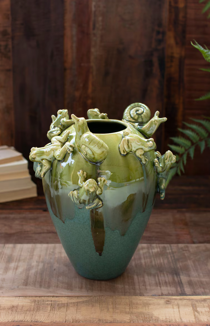 Green ceramic vase with fogs and snails with a background of wood panels
