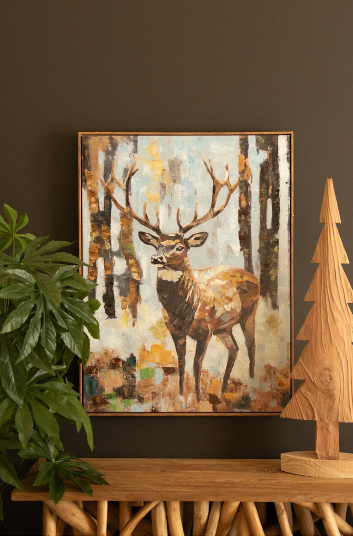 Framed artwork of a deer in a forest scene on a dark wall with decorative elements.