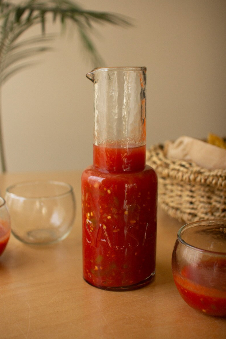 Jar of red salsa with a basket of chips next to it
