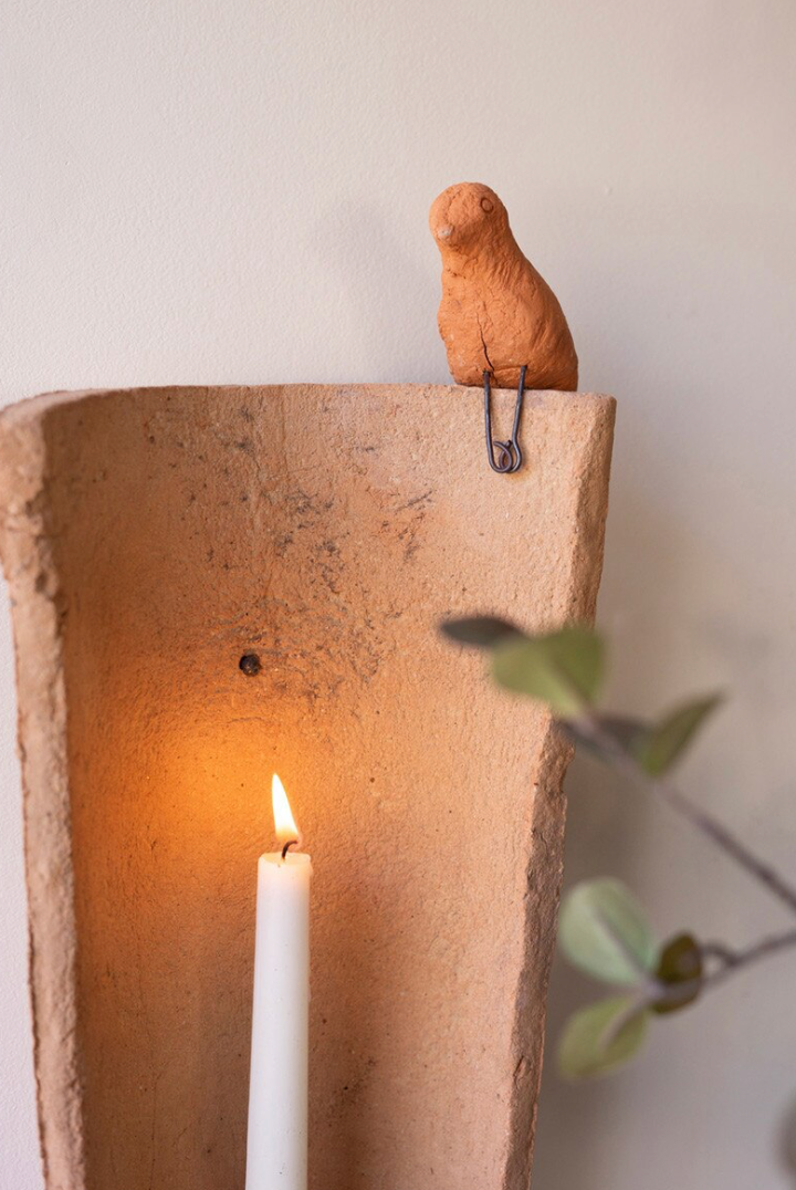 close up of small clay bird perched on top of tile.