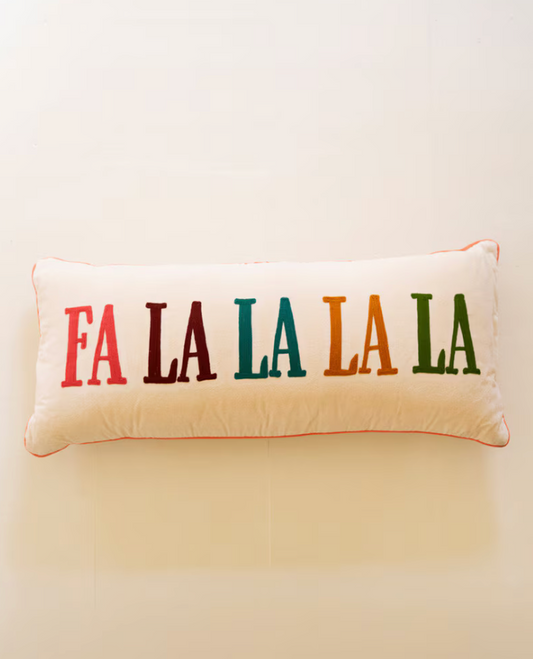 A rectangular cream throw pillow with the phrase 'FA LA LA LA LA' embroidered across the front in multicolored serif letters, set against a plain cream background.
