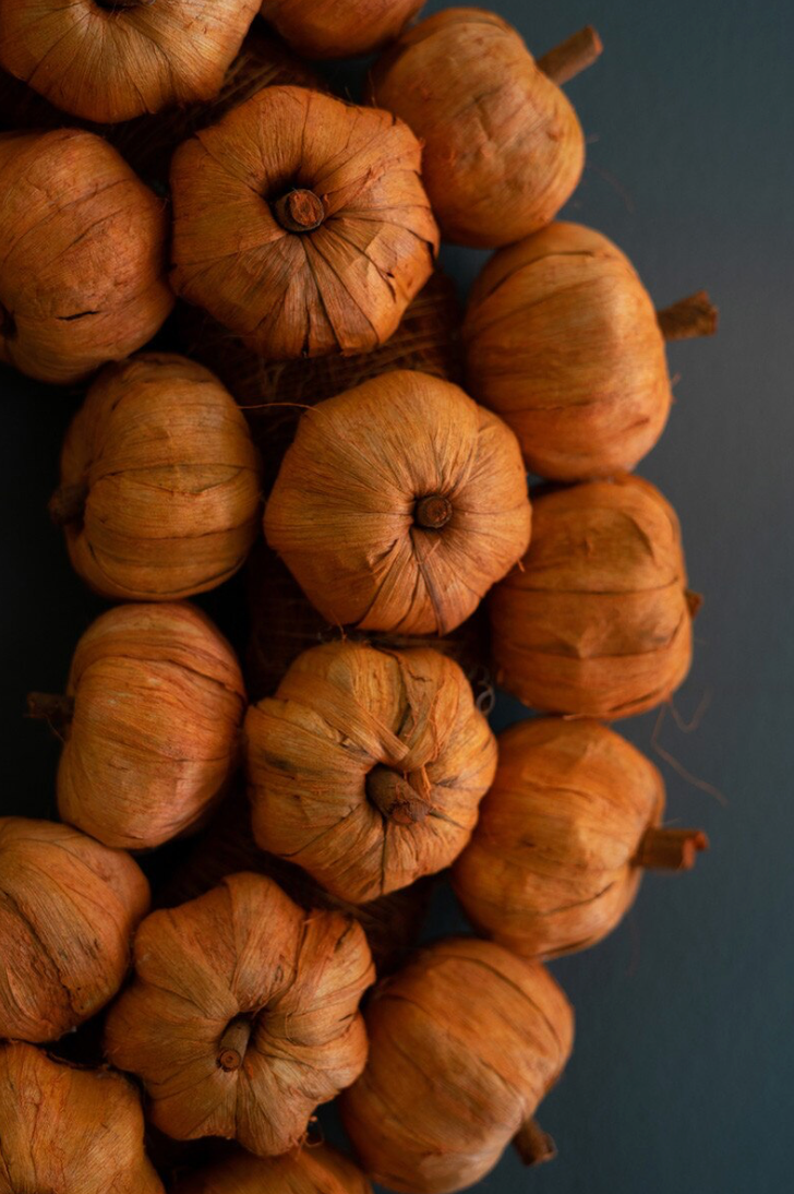 A cluster of small dried decorative pumpkins or gourds in warm tan and brown tones, arranged closely together against a dark blue-gray background.