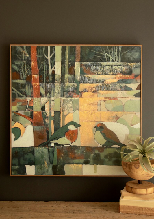 A framed abstract bird painting hangs on a dark wall above a wooden surface, with a potted plant and books beside it. The artwork features two birds in a patchwork-style scene with muted greens, beige, orange, gray, and white tones.