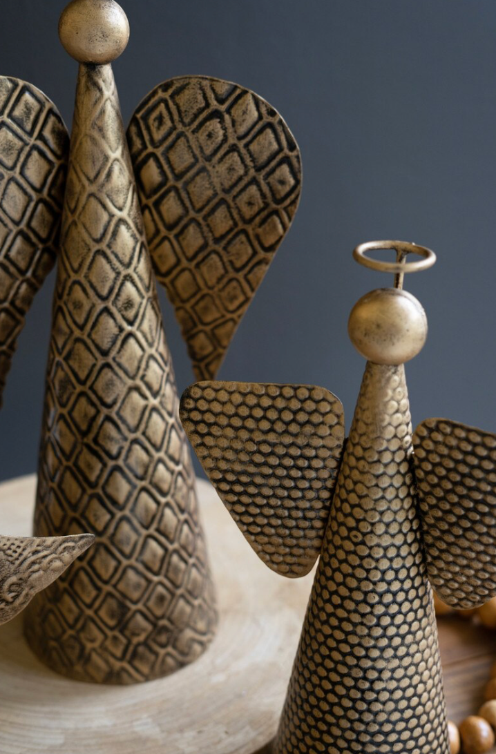 Decorative angel-shaped ornaments with textured metallic wings and cone bodies, displayed on a wooden surface against a dark gray background.