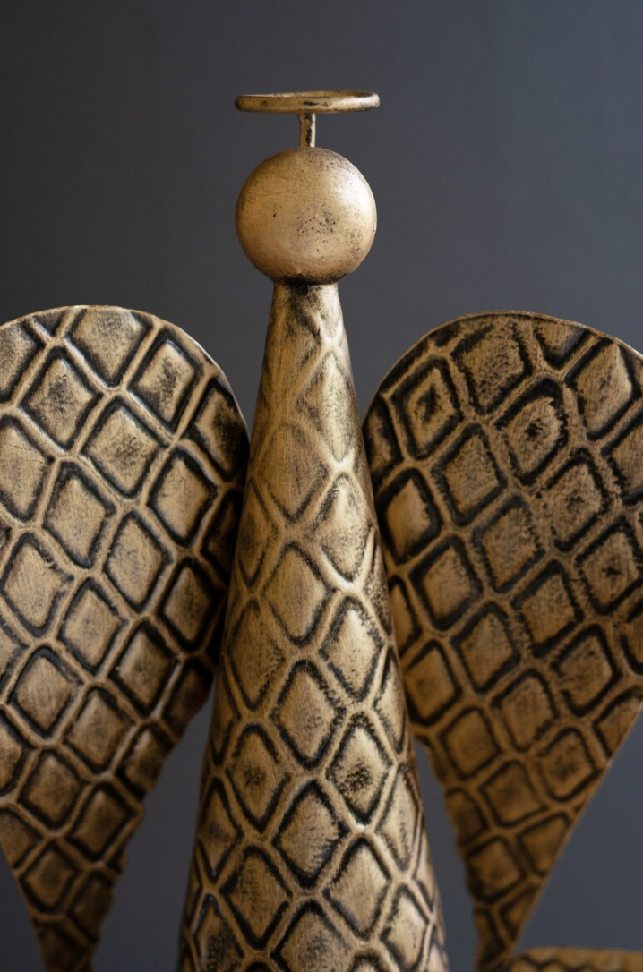 A close-up of a sculptural decorative object with a textured metallic gold finish, featuring a central cone-like form with a circular top and two curved wing-like sides with a repeating diamond pattern, set against a dark gray background.