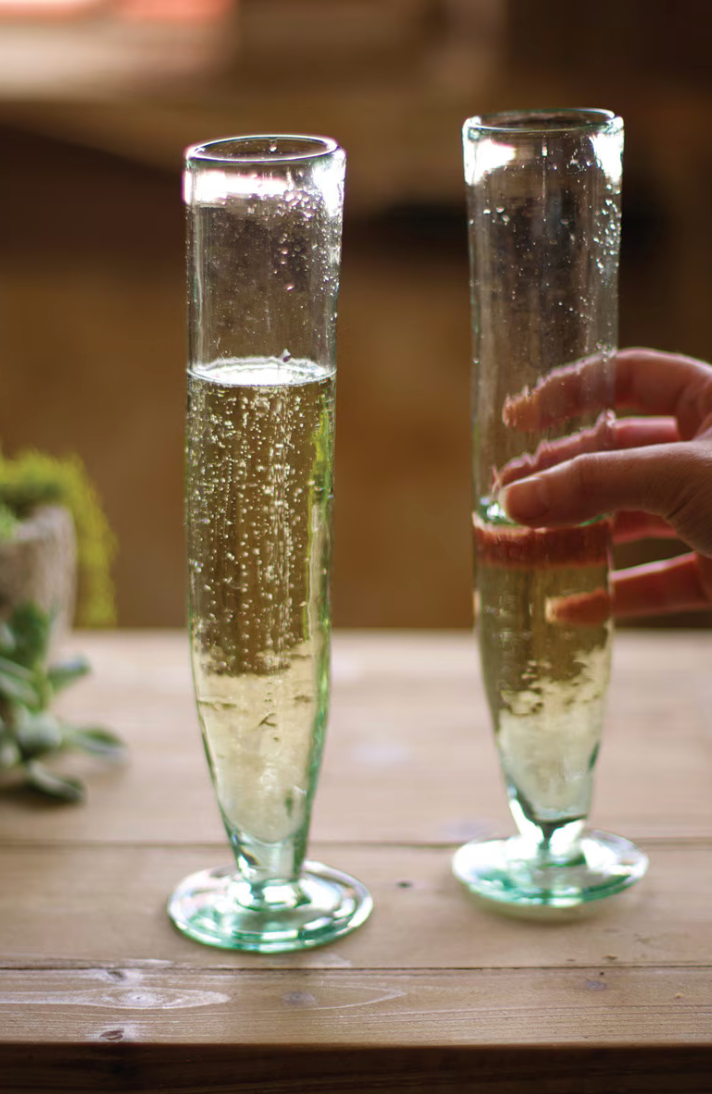 Two clear glass flutes filled with bubbly champagne on a wooden table, with a hand holding the right glass.
