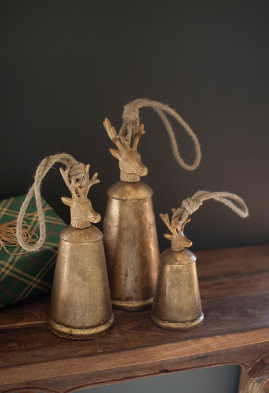 Three vintage-style brass bells with deer heads on a wooden surface against a dark background
