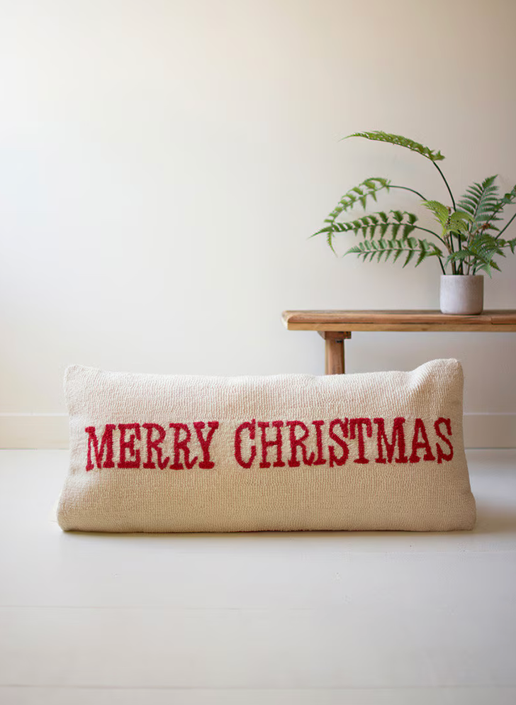 White pillow with red script reading Merry Christmas 
