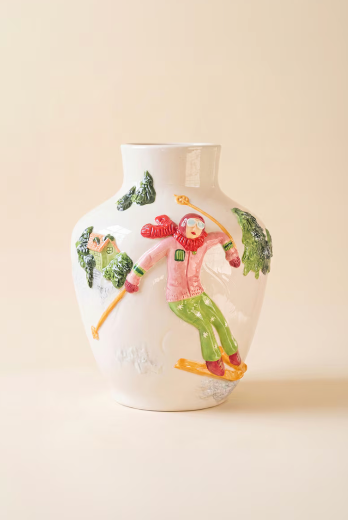 Ceramic Christmas Vase with Skier on woven rattan surface showing full skier design in pink jacket, green pants, yellow skis, and alpine cottage with pine trees in raised relief"