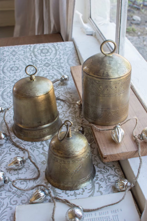 "Close-up detail of etched metal Christmas bell with antique brass finish showing intricate engraved pattern and warm patina, by Kalalou"