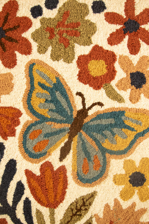 Close-up of a textured rug featuring a large blue and yellow butterfly surrounded by orange, brown, and yellow flowers on a cream background.