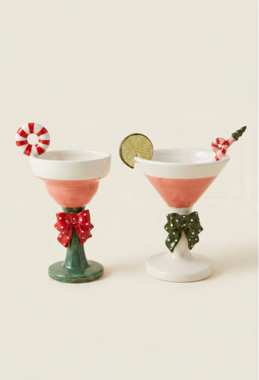 Two holiday-themed cocktail glasses with pink liquid, decorated with candy canes, a lime wheel, and red and green bows, set against a warm cream background.