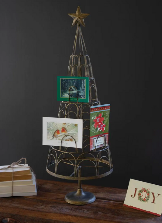 metal Christmas tree card holder with a star on top and room for 40 cards. Three cards on the tree and a book to the left and a card to the right on a wooden table.
