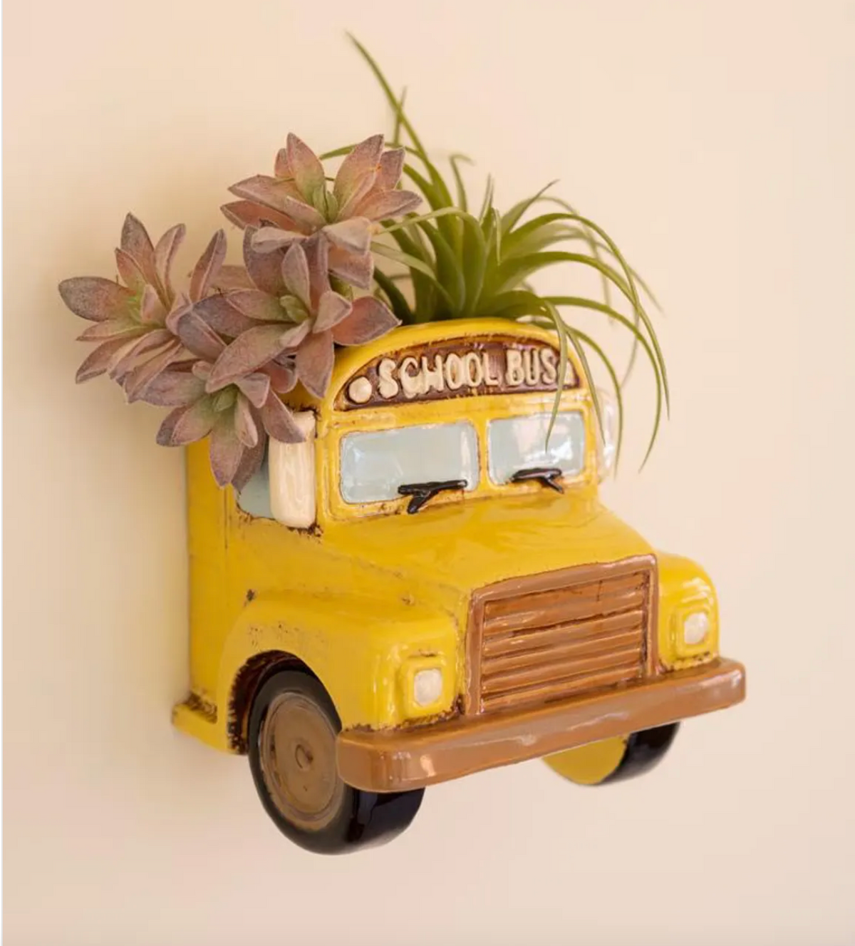 Yellow schoolbus attached to a all with succulents coming out of the top.
