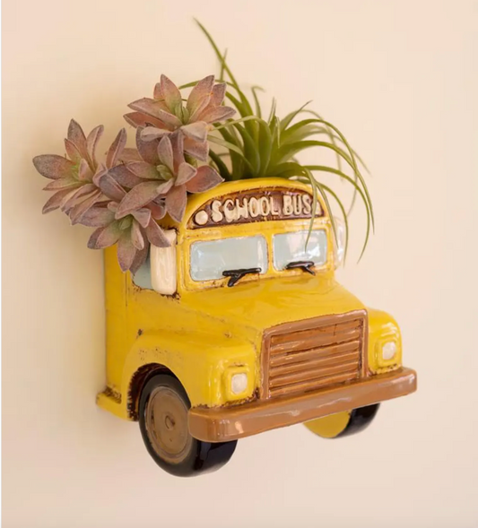 Yellow schoolbus attached to a all with succulents coming out of the top.
