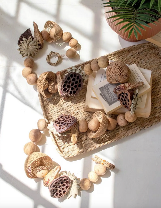 Dried mixed botanical garland in tan, cream, and brown arranged around a woven tray and open book.