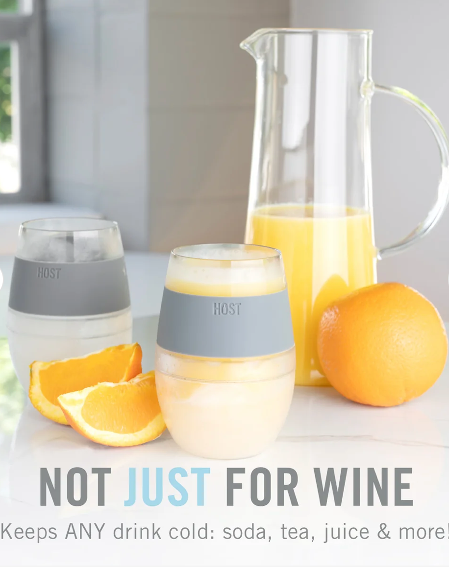 Two small HOST brand insulated drink chillsers with gray silicone bands are shown on a countertop with oranges and a glass pitcher of orange juice in a bright kitchen setting. Text at the bottom reads 'NOT JUST FOR WINE'.