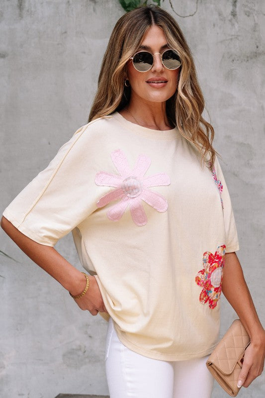 Woman wearing a beige t-shirt with floral designs against a gray wall.