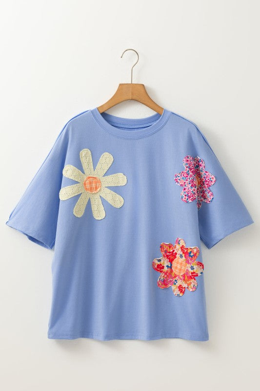 Blue t-shirt with floral designs on a wooden hanger against a white background