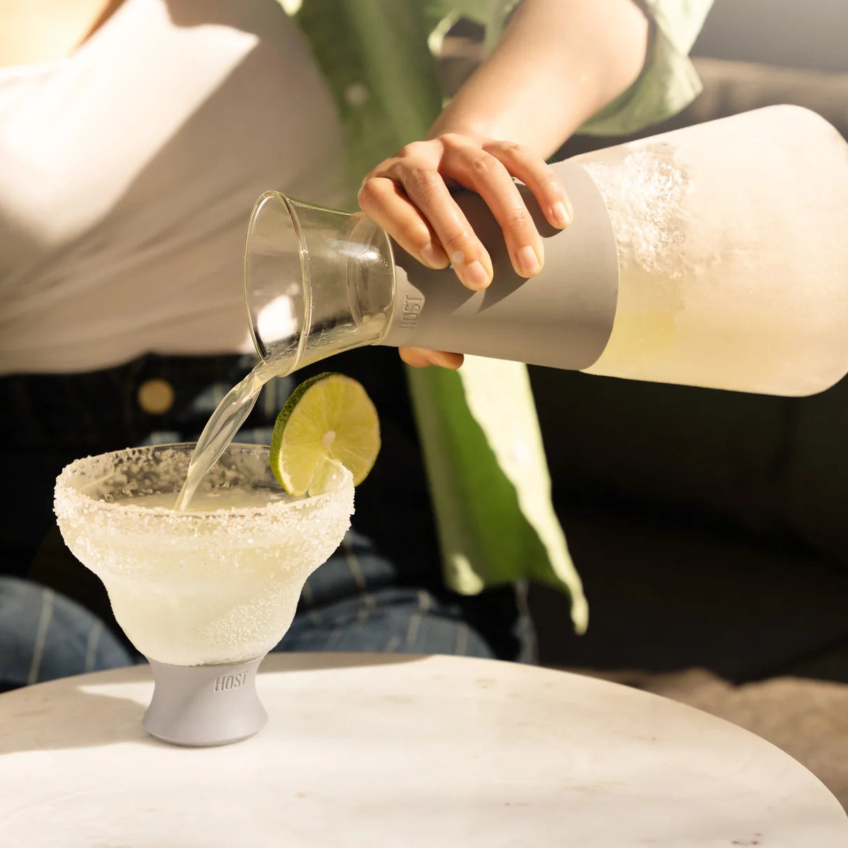Person pouring a drink into a glass with a lime wedge, using a bottle labeled 'HOUSN'.