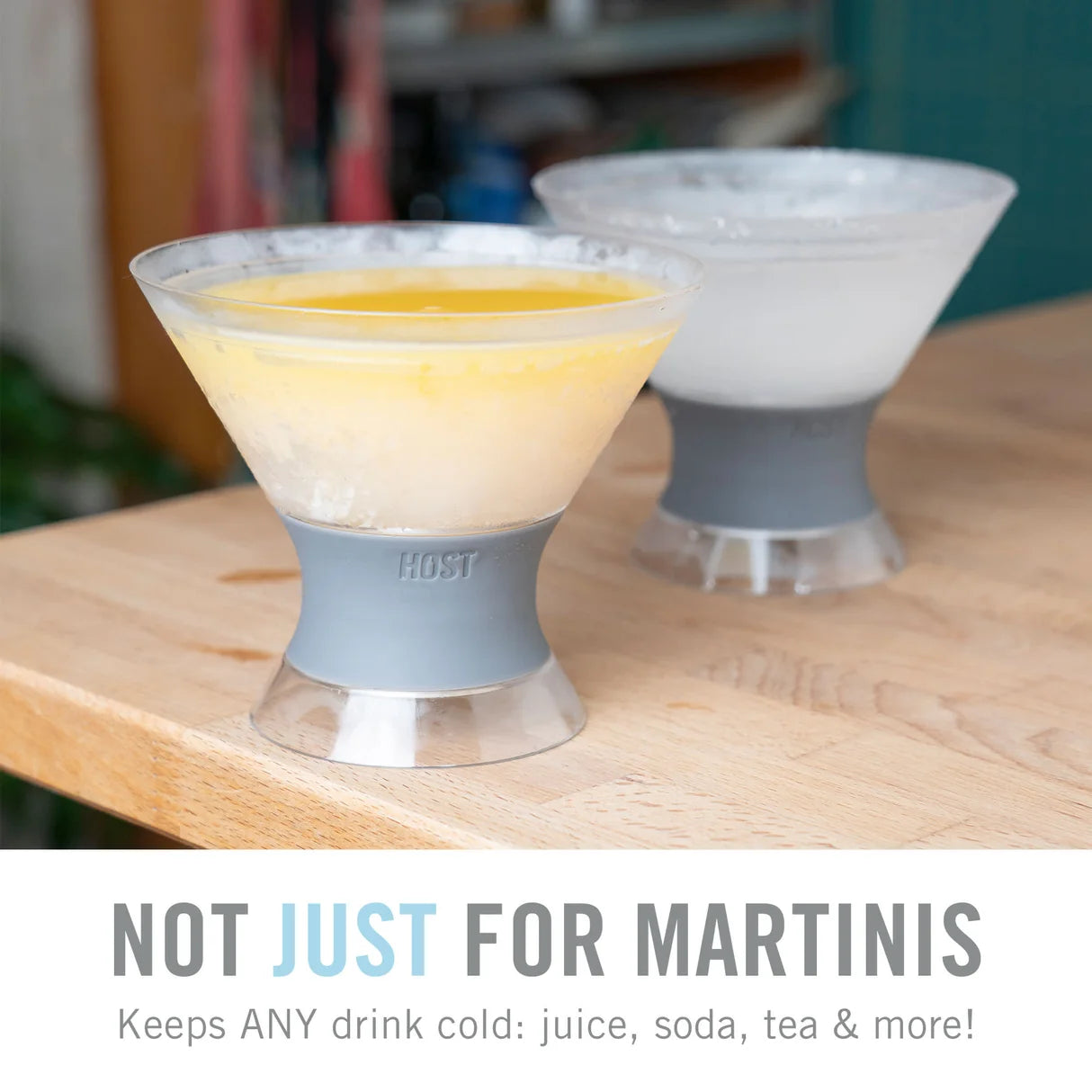 Two clear glass cocktail glasses with gray silicone bases sit on a wooden table. One glass contains a pale yellow drink and the other is empty, with a text banner at the bottom reading 'NOT JUST FOR MARTINIS'.