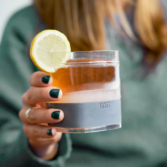 Person holding a cocktail with a lemon slice in a glass labeled 'HOST'.